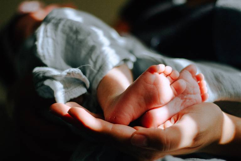 Fotografia mostra mão segurando pés de bebê