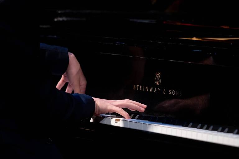 Em foto colorida, duas mãos aparecem em um teclado de piano