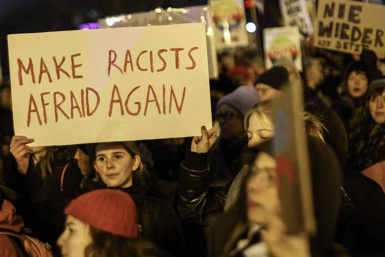 Uma mulher branca em uma manifestação segura uma placa onde se lê a frase "faça com que racistas tenham medo novamente" em inglês.