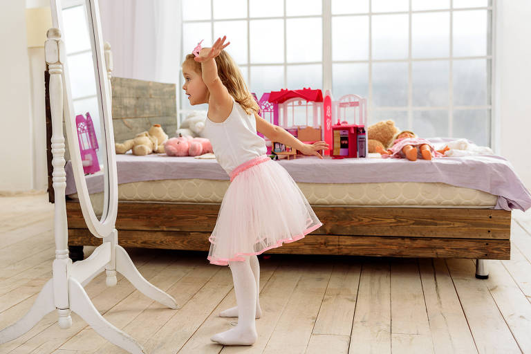 Uma menina loira com saia de balé em frente a um espelho