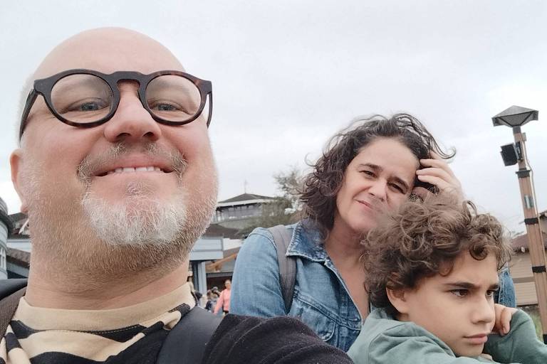 Um homem de óculos faz uma selfie mostrando ele, a mulher e o filho