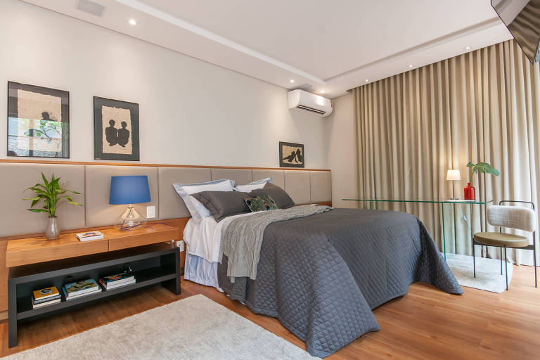 Quarto com cama de casal, piso de madeira e cabeceira de madeira com estofado em cinza