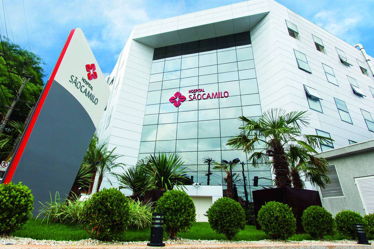 Fotografia colorida mostra a fachada do prédio branco espelhado, com o logo do Hospital São Camilo em vermelho