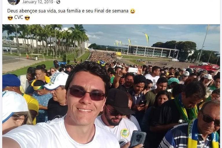 Homem de camisa branca e óculos escuros faz selfie em meio a pessoas vestidas de verde e amarelo