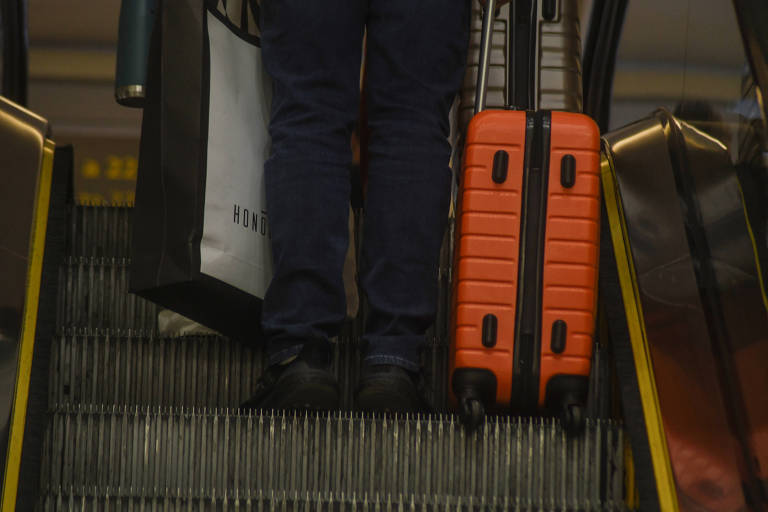 Imagem mostra passageiro com mala laranja em escada rolante