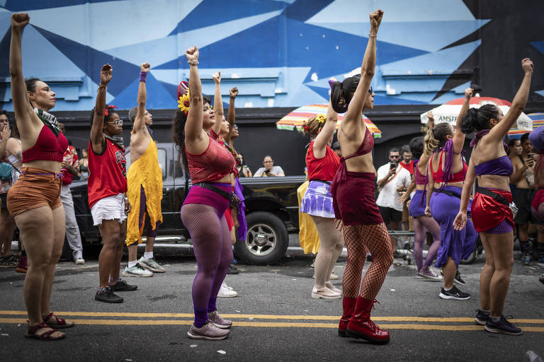 Mulheres de trajes carnavalescos levantam a mão com o punho fechado em uma coreografia