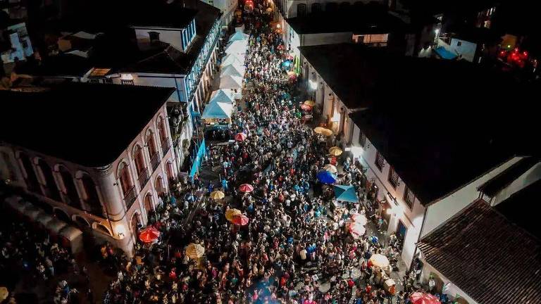 Uma rua tomada de gente, vista por cima. As pessoas dançam Carnaval e são ladeadas por casarões históricos