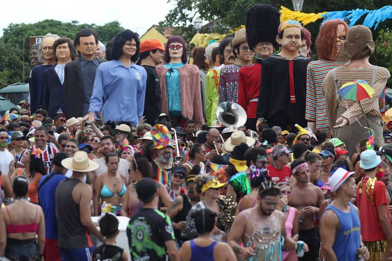 Uma aglomeração de pessoas de vários estilos acompanha uma fila de bonecos gigantes, com o personagem Kico, do Chaves; a cantora Rita Lee, o presidente da Argentina, Javier Milei, entre outros vários