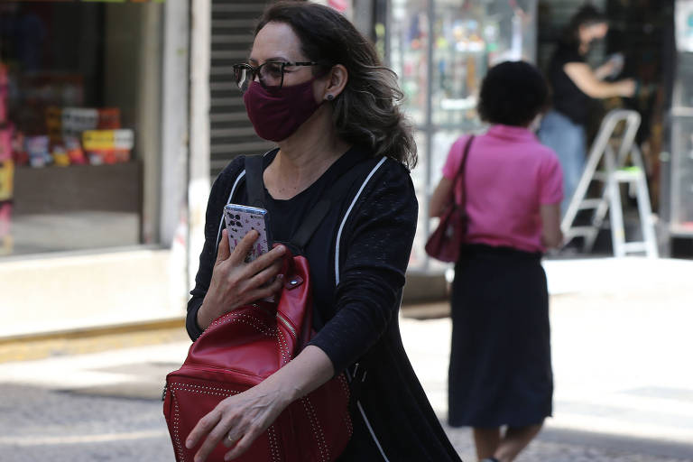Mulher com celular próximo ao peito, andando pela rua Conselheiro Crispiniano