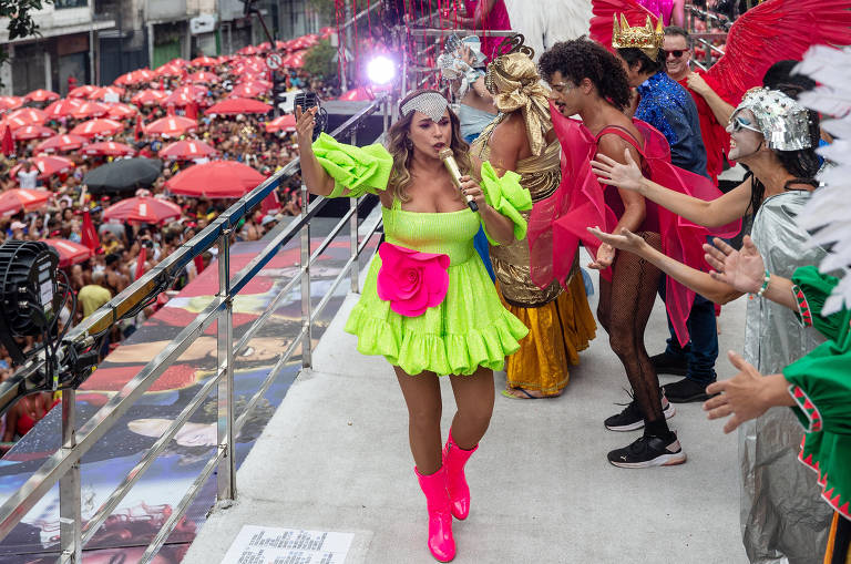 Cantora veste figurino verde neon, sapatos rosa e adereço prateado na cabeça.