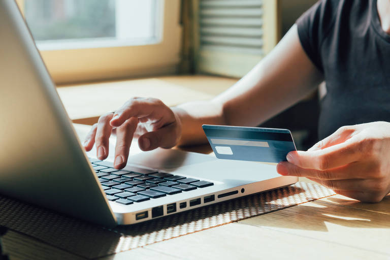 Garota faz uma compra na internet no computador com cartão de crédito