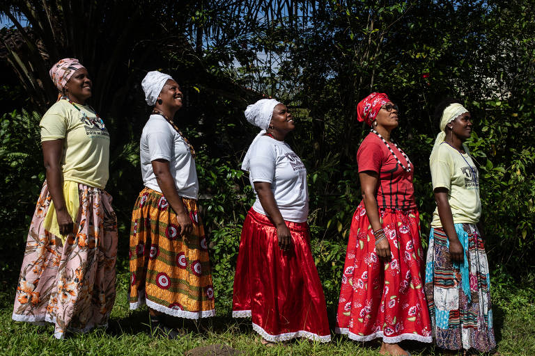 Foto mostra cinco mulheres em fileira por altura, de lado. Elas são negras e usam blusas do Rota da Liberdade, lenços na cabeça e saias longas e coloridas