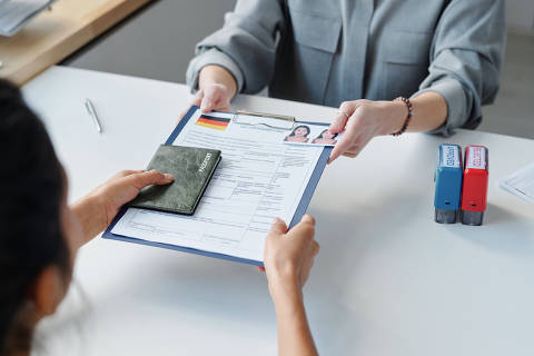 Vista de alto ângulo de mulher irreconhecível solicitando visto na embaixada dando passaporte e formulário de inscrição para especialista .(Foto: AnnaStills/Adobe Stock )