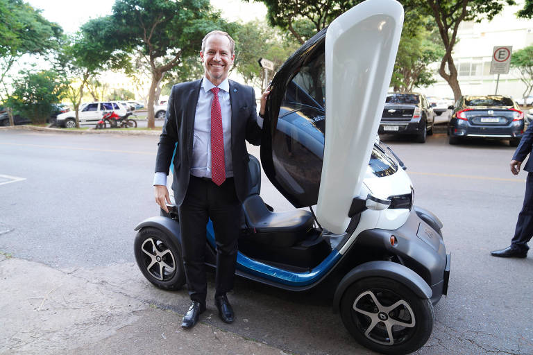 Homem está em pé segurando a porta de um carro pequeno. A porta abre para cima