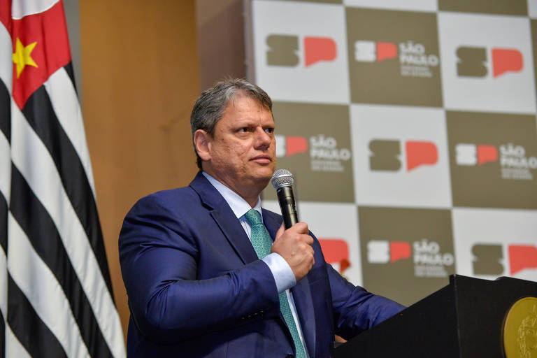 O governador de São Paulo, Tarcísio de Freitas, fala ao microfone tendo uma bandeira de São Paulo ao lado