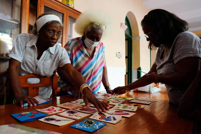 Mulheres negras idosas mexem em cartas espalhadas em uma mesa