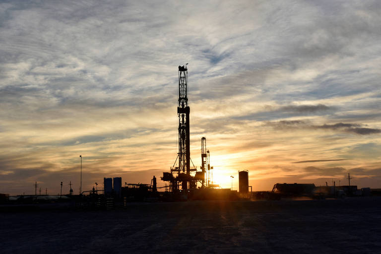 Equipamentos e torre de produção de petróleo vistos na hora do pôr do sol