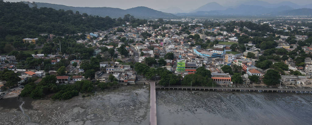 foto aérea mostra área densamente urbanizada, com muitas casas, alguns restos de vegetação e áreas verdes ao fundo, com morros e montanhas. em primeiro plano, pier 