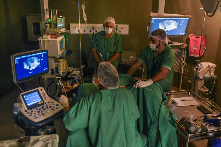 Imagem de sala de cirurgia onde está sendo realizada a coleta de óvulos, há 4 pessoas na foto, 3 médicos e uma paciente.