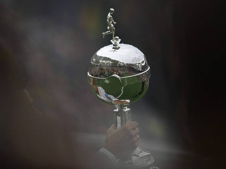 Homem não identificado segura o troféu da Libertadores, no Maracanã, antes da final da edição de 2023, entre Fluminense e Boca Juniors; ele é prateado e tem no topo um jogador em miniatura chutando uma bola