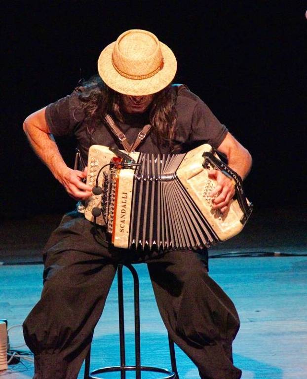 Em foto colorida, o músico aparece tocando seu instrumento a gaita-ponto