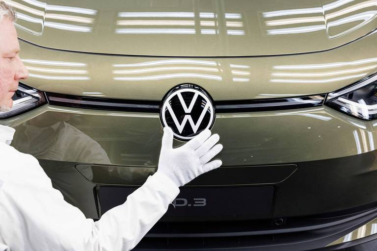 Empregando da Volkswagen em frente ao veículo elétrico ID 3, fabricado em Zwickau, na Alemanha. Ele usa jaleco e luva brancos.