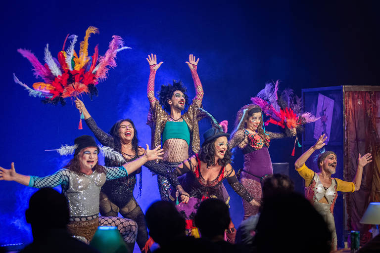 A imagem mostra artistas com roupas coloridas em um palco
