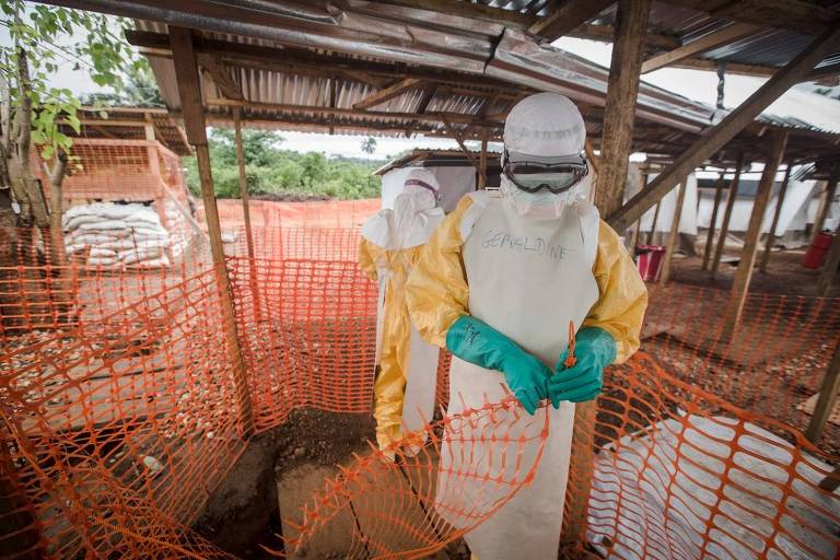 pessoas com trajes anti-ebola em barraco de madeira 