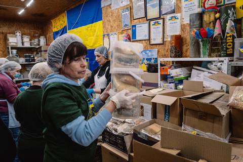 Kyiv, Ucrânia - 17/4/2024 -   Voluntária carrega pilha de potes com alimentos desidratados na sede do projeto 