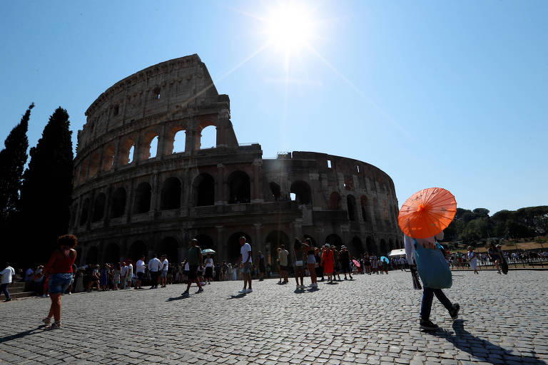 Pessoa usa guarda-chuva laranja para se proteger do sol forte em frente ao Coliseu