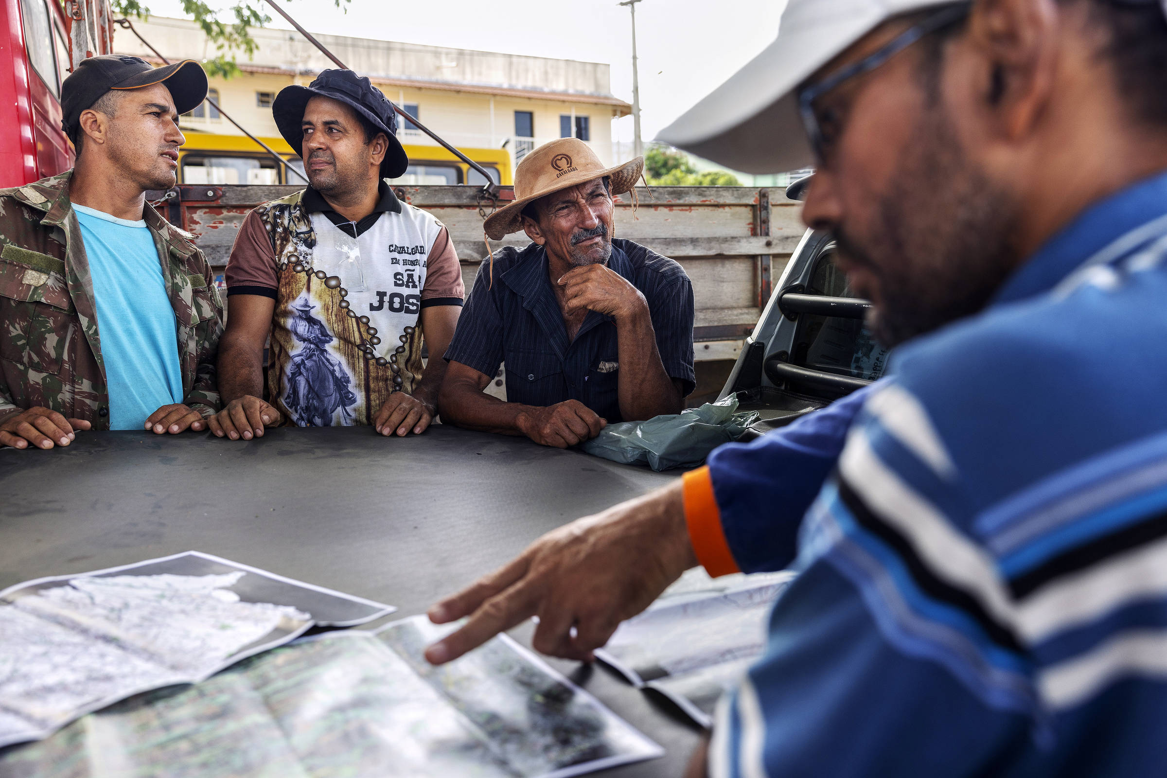 Agricultores observam mapas estendidos na caçamba de uma caminhonete