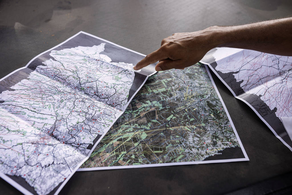 Uma mão aponta para três mapas abertos sobre a lona da caçamba de uma caminhonete 