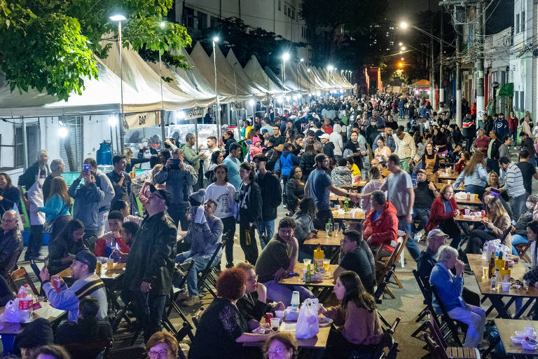 Pessoas estão sentadas em mesas na rua