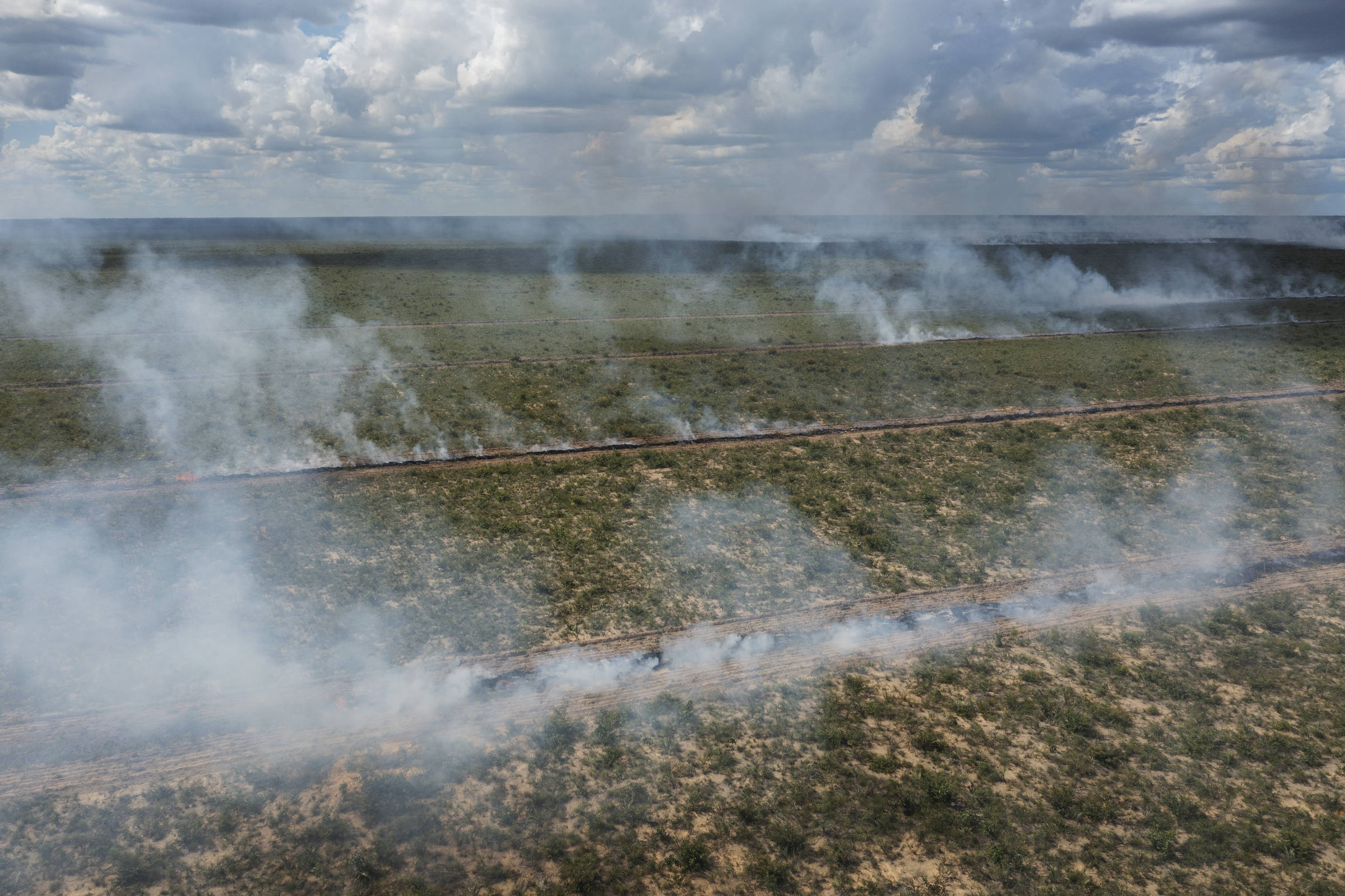 Vista aérea de leiras, que são pilhas de raízes e troncos de árvores, sendo queimadas em região de cerrado desmatada