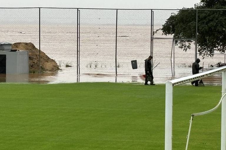  O Centro de Treinamento Parque do Gigante, do Internacional, inundado. Dois homens seguram rodos perto de uma grade.