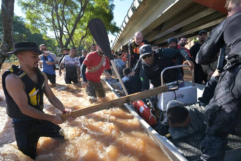 Na foto, um homem dentro da água bate em uma pessoa dentro de um barco com um pedaço de pau