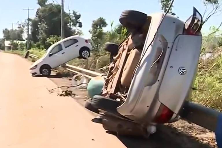 Na foto, dois carros estão revirados em uma estrada suja