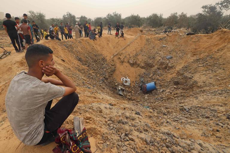 Palestinos próximos de cratera formada pelo impacto de ataque aéreo israelense na região de Rafah, na Faixa de Gaza