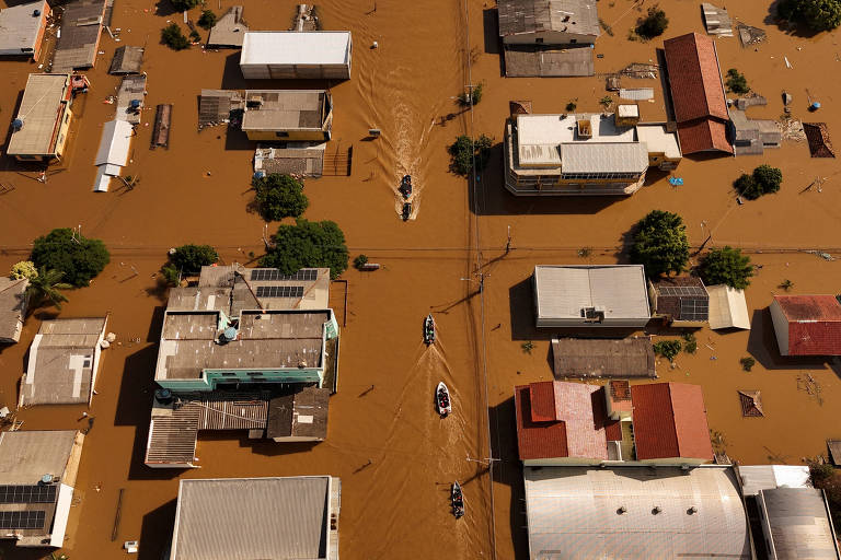 Foto aérea mostra telhados de casas em região alagada por água marrom