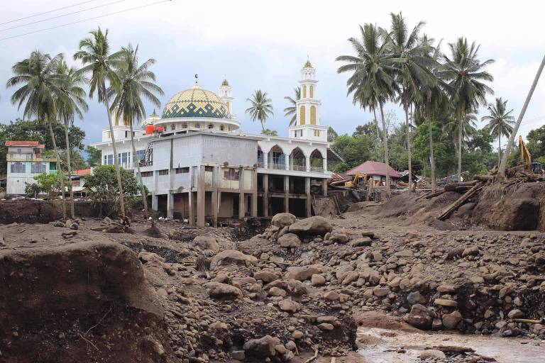 Pilhas de escombros e lama tomam conta de uma rua em Tanah Datar, ao fundo podemos ver uma mesquita cercada por palmeiras.