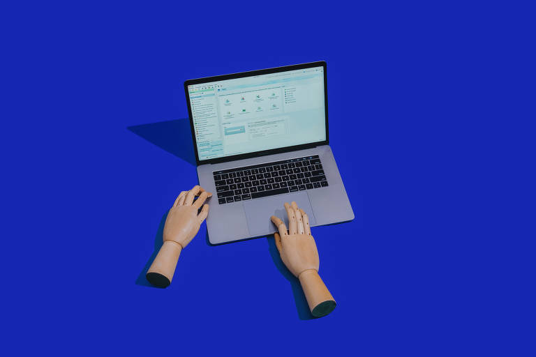 Na fotografia, um fundo azul marinho, um notebook cinza aberto e ligado com duas mãos de manequim simulando que estão mexendo acessando o aparelho.