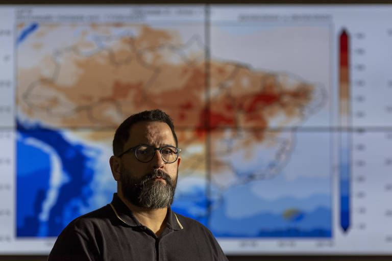 homem pardo, de barba e óculos, tendo ao fundo um mapa meteorológico