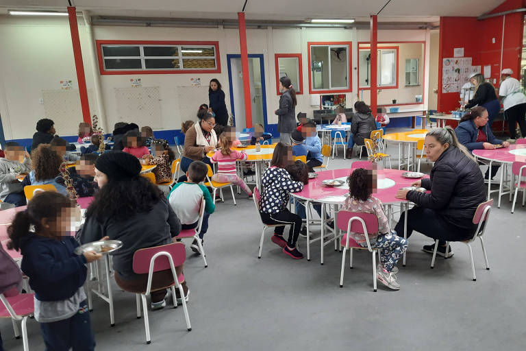 Na foto, crianças almoçam em mesas circulares no pavilhão de uma escola