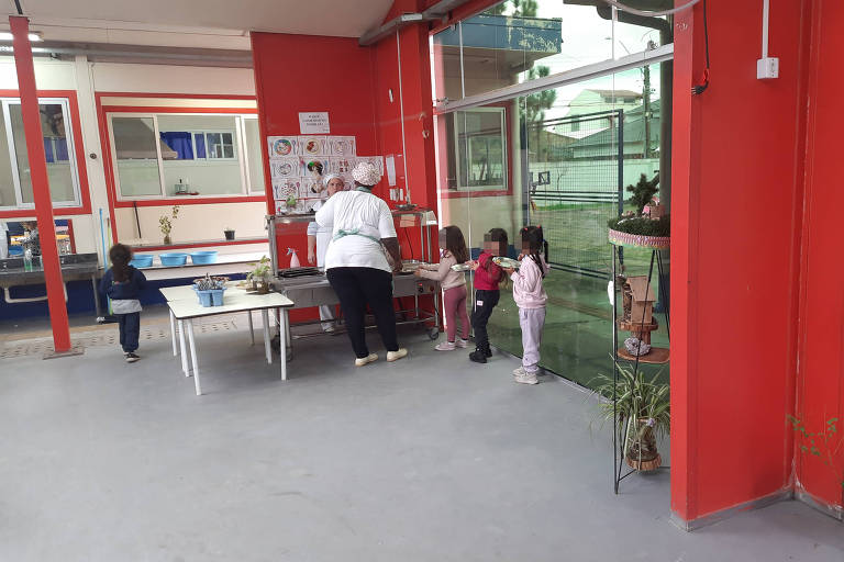 Na foto, crianças fazem uma pequena fila em frente ao buffet da escola