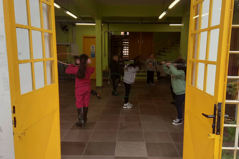 Na foto, crianças dentro de uma escola brincam com bambolês