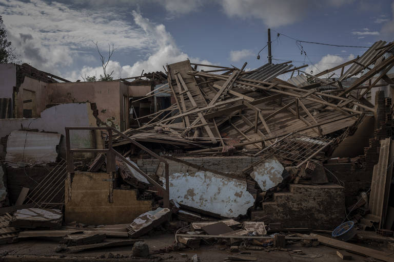 A imagem captura os escombros de uma construção após a enchente em São Sebastião do Caí. Madeiras quebradas, telhas e pedaços de metal estão espalhados em desordem