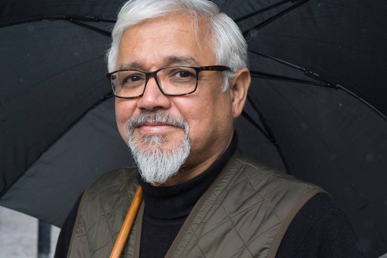 homem indiano de óculos e cabelo branco segura um guarda-chuva acima de si
