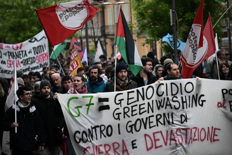Pessoas seguram um cartaz onde se lê 'G7 = genocício greenwashing. Contra governantes da guerra e da devastação'