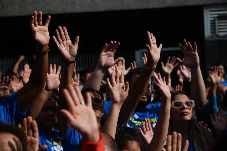 Pessoas levantam as mãos para o alto durante a Marcha para Jesus em São Paulo; alguns deles vestem camisa azul