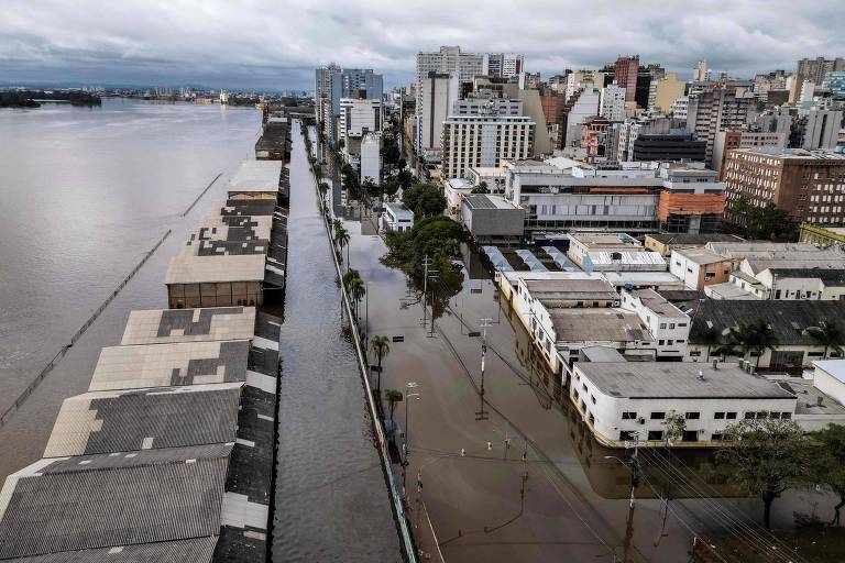 Vista aérea de ruas alagadas ao lado da orla do lago Guaíba; o dia está nublado